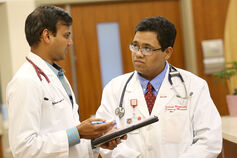 A medical professional holding a tablet speaks with a medical student.